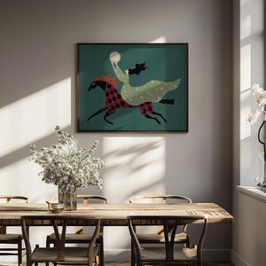 May include: A framed art print depicts a figure riding a horse across a teal background. The horse is red and black checkered, and the rider wears a green dress and holds a white orb. The artwork is displayed above a wooden dining table.