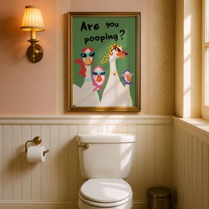 May include: A framed art print with the text "Are you pooping?" above a whimsical illustration of three geese wearing sunglasses and scarves. The artwork hangs above a white toilet in a bathroom setting.