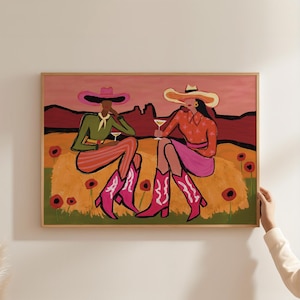 Puede incluir: Una impresión artística enmarcada representa a dos figuras con sombreros y botas de vaquero, disfrutando de cócteles. La obra de arte presenta una paleta de colores vibrantes de rosa, naranja, verde y rojo, con un fondo de paisaje desértico y detalles florales.