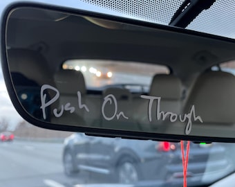 May include: A rearview mirror with the words "Push On Through" written in white marker on the surface. A red string hangs from the mirror.