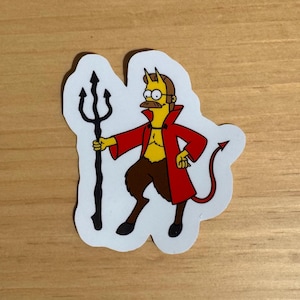 Peut inclure: Autocollant représentant un personnage de diable de dessin animé. Le diable porte un manteau rouge, a la peau jaune, des jambes marron et tient un trident noir. Le personnage a une moustache, des lunettes et des cornes.