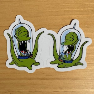 Puede incluir: Dos pegatinas de extraterrestres verdes con una cara gritando en una cúpula de vidrio. Los extraterrestres tienen cuatro tentáculos y llevan un collar a rayas azul y naranja.