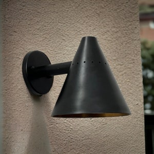 May include: Black wall-mounted light fixture with a cone-shaped shade. The shade has a gold interior and small holes.