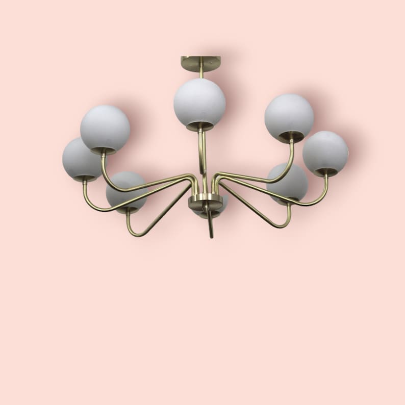K&ouml;nnte beinhalten: Ein goldener Kronleuchter mit sieben wei&szlig;en, kugelf&ouml;rmigen Gl&uuml;hbirnen. Der Kronleuchter hat ein modernes Design mit geschwungenen Armen.