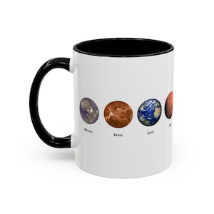 May include: White ceramic mug with a black rim and handle. The mug features a graphic of the planets Mercury, Venus, Earth, and Mars with their names printed below each planet.