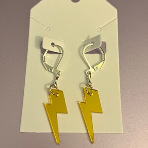 May include: A pair of silver earrings with gold lightning bolt charms. The earrings are on a white card.