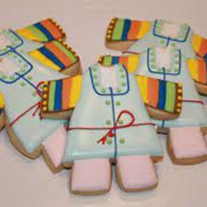 May include: Six decorated sugar cookies shaped like a baby onesie. The cookies are light blue with white buttons and a red bow. The sleeves are decorated with stripes of yellow, orange, green, and blue.