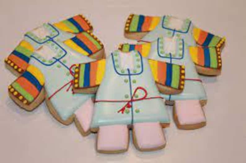 May include: Six decorated sugar cookies shaped like a baby onesie. The cookies are light blue with white buttons and a red bow. The sleeves are decorated with stripes of yellow, orange, green, and blue.