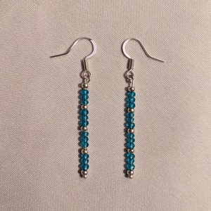 May include: A pair of silver dangle earrings with a long strand of turquoise blue crystal beads.
