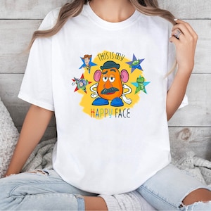 May include: White t-shirt featuring a colourful graphic of Mr. Potato Head and the text "This is my Happy Face".