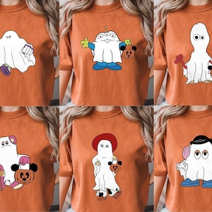 Puede incluir: Seis camisetas naranjas con diferentes diseños de fantasmas con temática de Halloween. Cada fantasma sostiene una calabaza de Halloween.
