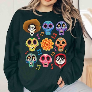 May include: Dark green sweatshirt with a colorful print of a skeleton character from the movie Coco. The print includes a variety of colorful sugar skulls and musical notes.