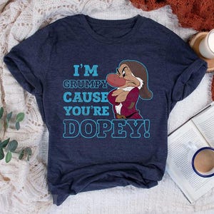 Puede incluir: Una camiseta azul marino con un gráfico de Grumpy de Blancanieves. El texto en la camiseta dice "I'm Grumpy Cause You're Dopey!"