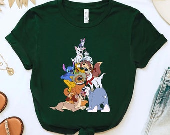 May include: A green t-shirt with a graphic print of a group of cartoon dogs and Stitch from Lilo & Stitch. The dogs are stacked on top of each other in a pyramid shape.