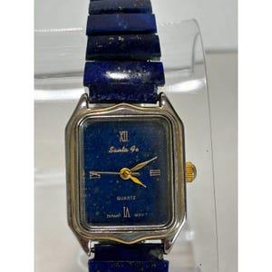 May include: A rectangular Santa Fe quartz watch with a dark blue face and a silver-colored metal case. The watch has gold-colored hands and a dark blue lapis lazuli band. The watch face displays the text "Santa Fe" and "Quartz".