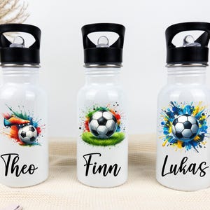 Puede incluir: Tres botellas de agua blancas con tapas negras y diseños coloridos de fútbol. Las botellas están etiquetadas con "Theo", "Finn" y "Lukas".
