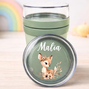 Op de afbeelding: Een groene en doorzichtige reismok met een deksel met een hertenillustratie en de naam "Malia". De beker heeft een groene siliconen band. Het ontwerp is gelabeld "Design 3".