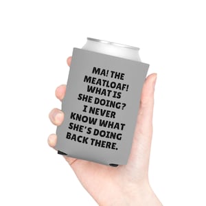 May include: A gray can cooler with the text "MA! THE MEATLOAF! WHAT IS SHE DOING? I NEVER KNOW WHAT SHE'S DOING BACK THERE." in black. The cooler is designed to keep beverages cold.