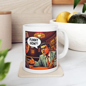 Puede incluir: Taza de cerámica blanca con una ilustración cómica de dos hombres en un bar. Un hombre gesticula con las manos, con el texto "FUNNY HOW?!" en un bocadillo. El otro hombre lleva un sombrero.