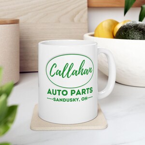 Puede incluir: Taza de cerámica blanca con un logotipo ovalado verde que dice "Callahan Auto Parts - Sandusky, OH" en texto verde.