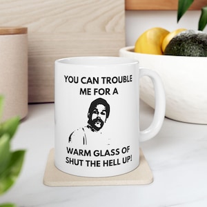 May include: White ceramic mug with a black and white image of a man with the text "You can trouble me for a warm glass of shut the hell up!"