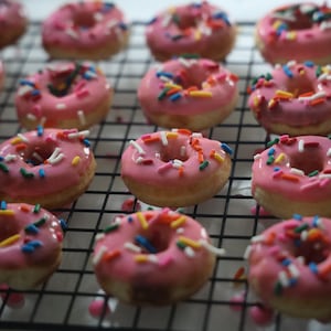Könnte beinhalten: Nahaufnahme eines Drahtgestells mit rosafarbenen, mit bunten Streuseln bestreuten Donuts.