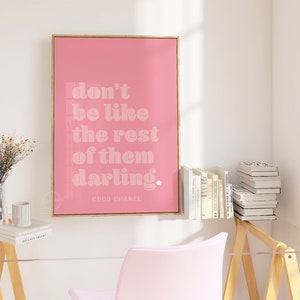 Puede incluir: P&oacute;ster enmarcado en rosa con una cita en blanco que dice "no seas como los dem&aacute;s, querida". La cita se atribuye a Coco Chanel.