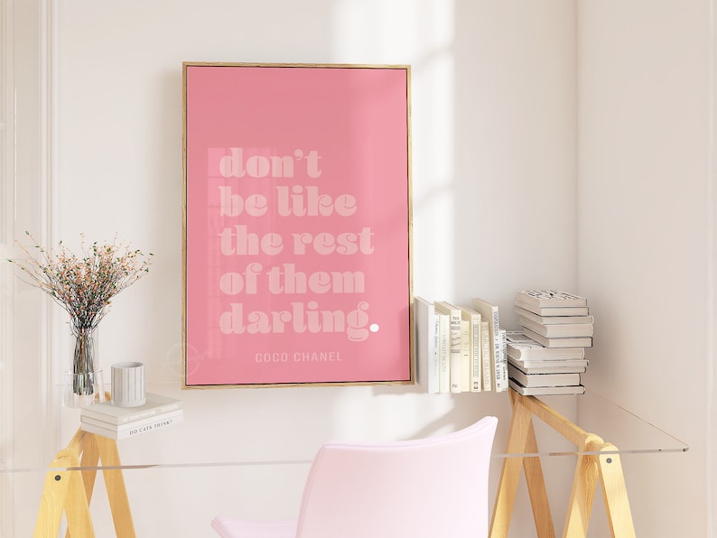 Puede incluir: P&oacute;ster enmarcado en rosa con una cita en blanco que dice "no seas como los dem&aacute;s, querida". La cita se atribuye a Coco Chanel.