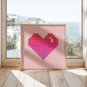 Pode incluir: Uma impressão emoldurada rosa com um design de coração pixelado em tons de vermelho e rosa.