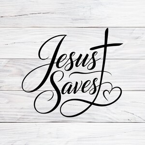 May include: A black vinyl decal featuring the text Jesus Saves in a flowing cursive script. The letter S in Saves extends upwards to form a cross, and a small heart is integrated into the tail of the letter s, all set against a white wood background.