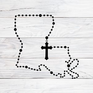 May include: Black rosary beads in the shape of the state of Louisiana, with a cross pendant. The beads are arranged to outline the state's borders, creating a unique religious symbol on a white wood-grain background.