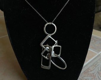 May include: A silver necklace with a geometric pendant featuring multiple interlocking circles and squares.