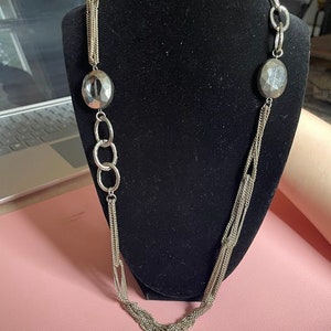 May include: A silver multi-strand necklace with two large oval-shaped silver beads. The necklace is displayed on a black velvet mannequin.