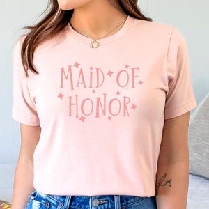 May include: A pink t-shirt with the text "Maid of Honor" in pink lettering with small pink stars around the text.