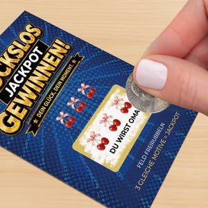 May include: A blue scratch-off lottery ticket with gold lettering that says "JACKPOT GEWINNEN!" and the text "DEIN GL&Uuml;CK, DEIN MOMENT." The ticket features cherry graphics and the text "DU WIRST OMA."