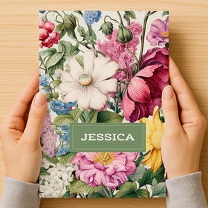 Peut inclure: Un carnet à motifs floraux avec un design vibrant présentant une variété de fleurs dans les tons de rose, rouge, jaune et bleu. Le carnet porte le nom "JESSICA" imprimé sur une étiquette rectangulaire verte.