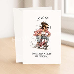 May include: A white greeting card with a cartoon illustration of a woman riding a pink tricycle. The text "HALLO 40" and "ERWACHSENWERDEN IST OPTIONAL" are printed on the card. The card is accompanied by a white envelope.
