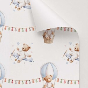 May include: Wallpaper featuring a repeating pattern of light brown teddy bears in white pajamas. Some bears fly in light blue airplanes, while others sit in hot air balloons with blue and white stripes. A string of colorful tassels connects the balloons.