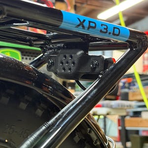 May include: Black bicycle rack with a blue and black stripe that reads "XP 3.D". The rack is mounted on a black tire. A black light is attached to the rack.