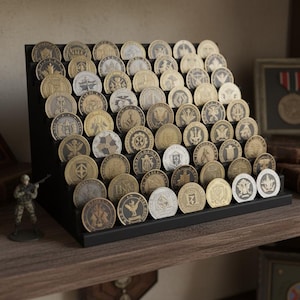 May include: A black display stand filled with numerous collectible coins, each featuring unique designs and emblems. The coins are arranged in rows, showcasing a variety of colors and finishes. Miniature military figures and framed memorabilia are also visible.