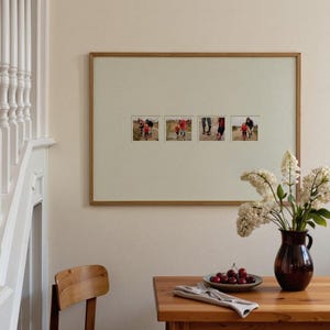 Peut inclure: Une œuvre d'art encadrée avec quatre petites photographies est affichée sur un mur. Le cadre est de couleur marron clair. Une table en bois contient un vase de fleurs blanches, une assiette de cerises et une serviette pliée.