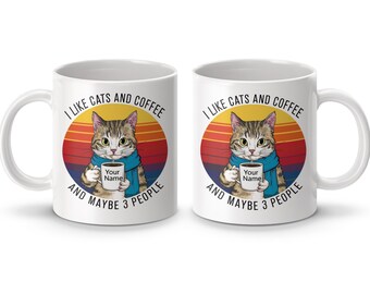 Könnte beinhalten: Weiße Keramik-Kaffeetasse mit einem bunten Retro-Design, das eine Katze zeigt, die eine Kaffeetasse hält. Der Text auf der Tasse lautet "Ich mag Katzen und Kaffee und vielleicht 3 Leute".