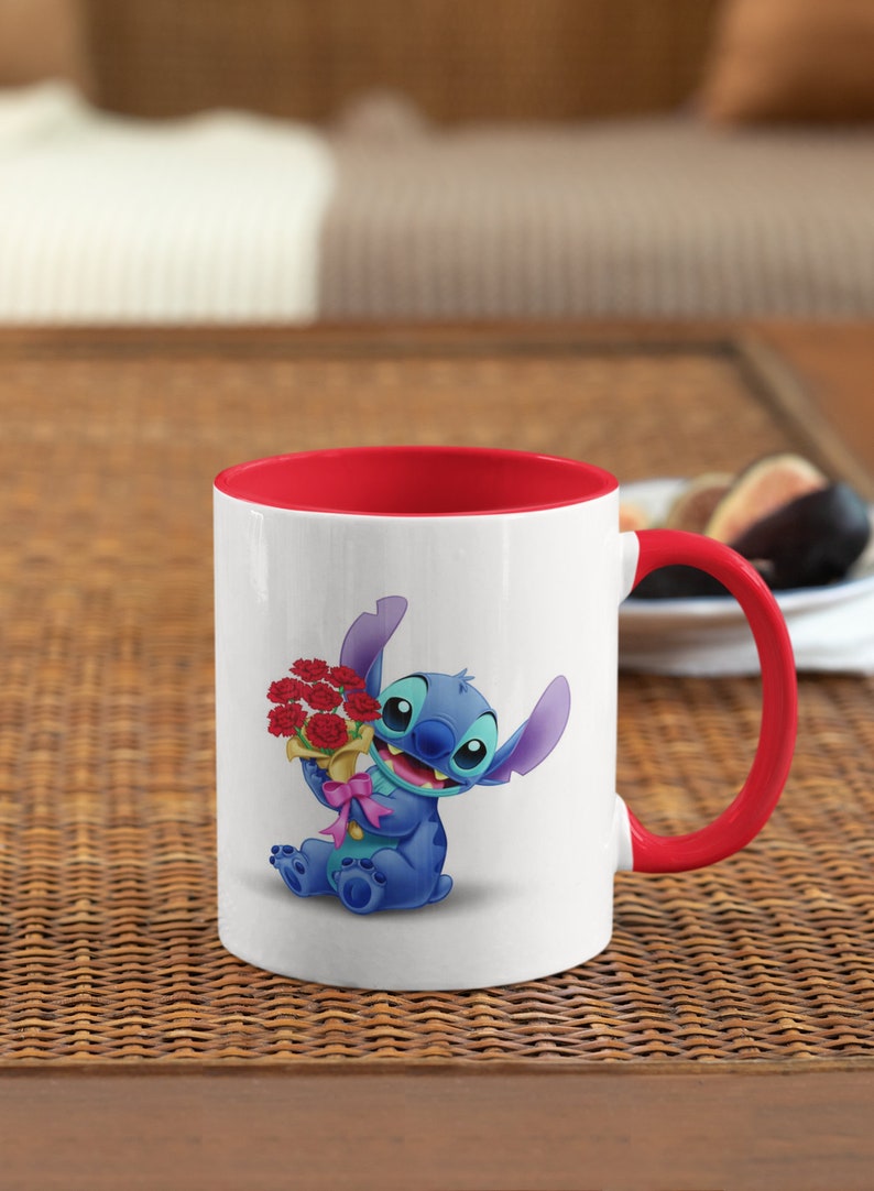 May include: White ceramic mug with a red rim and handle. The mug features a cartoon image of Stitch from Lilo & Stitch holding a bouquet of red flowers.