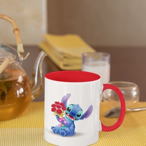 May include: A white ceramic mug with a red rim and handle. The mug features a cartoon image of Stitch from Lilo & Stitch holding a bouquet of red flowers.