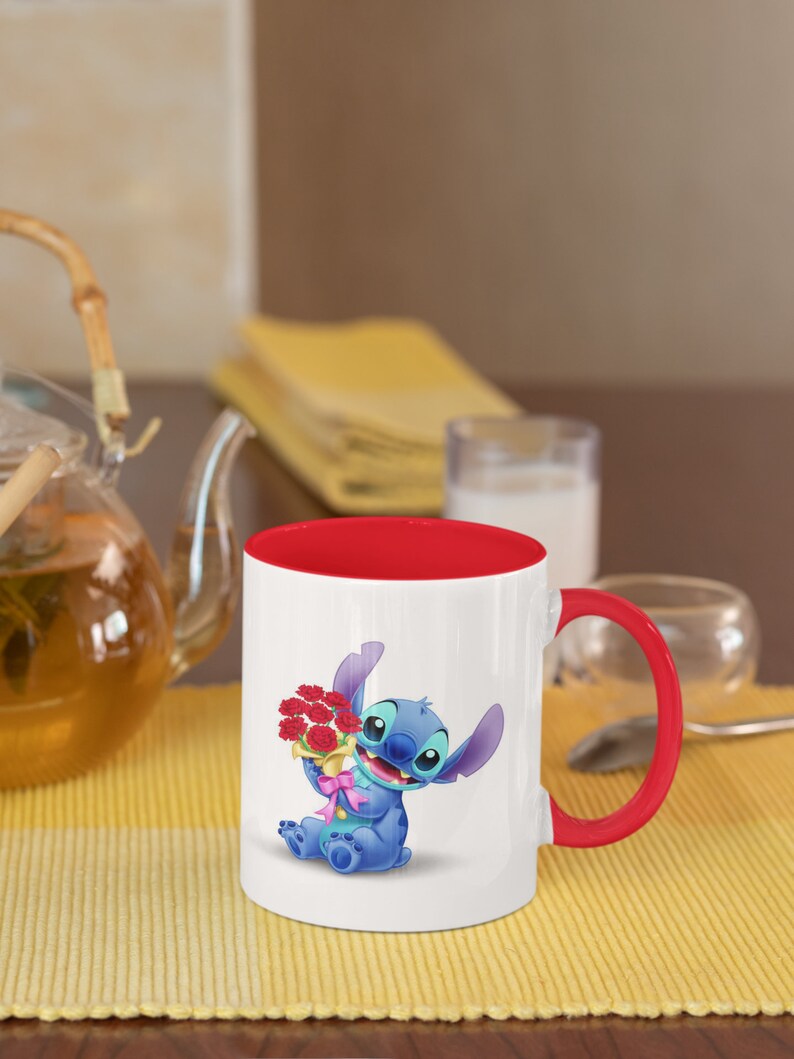 May include: A white ceramic mug with a red rim and handle. The mug features a cartoon image of Stitch from Lilo & Stitch holding a bouquet of red flowers.