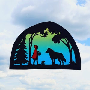 Può includere: Una figura rossa con cappuccio e un cestino cammina attraverso una foresta con un lupo. La scena è rappresentata in una silhouette colorata su uno sfondo sfumato blu e verde.