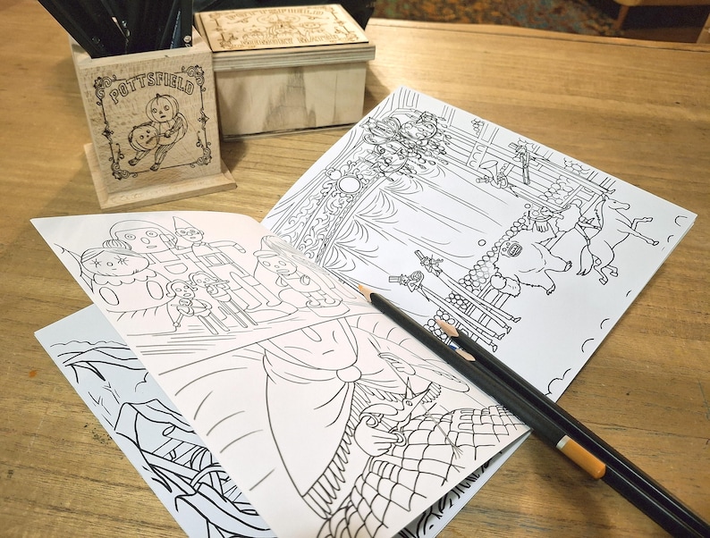 May include: A set of three coloring books with black and white illustrations. The books are open to pages depicting a carousel, a group of people, and a forest scene. The books are on a wooden table with two pencils.
