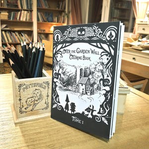 May include: A black and white coloring book titled "Over the Garden Wall Coloring Book, Tome I". The cover features a black and white illustration of a house in a forest with a character in a hooded cloak.