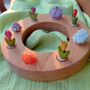 Puede incluir: Un expositor circular de madera con tulipanes de madera tallada en rosa, amarillo y rojo, y varios cristales. El expositor está sobre un fondo verde claro.