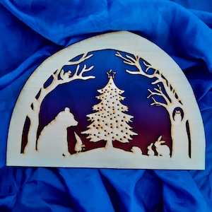 May include: A wooden cutout of a winter scene with a bear, a Christmas tree, and rabbits. The background is a gradient of blue and purple.